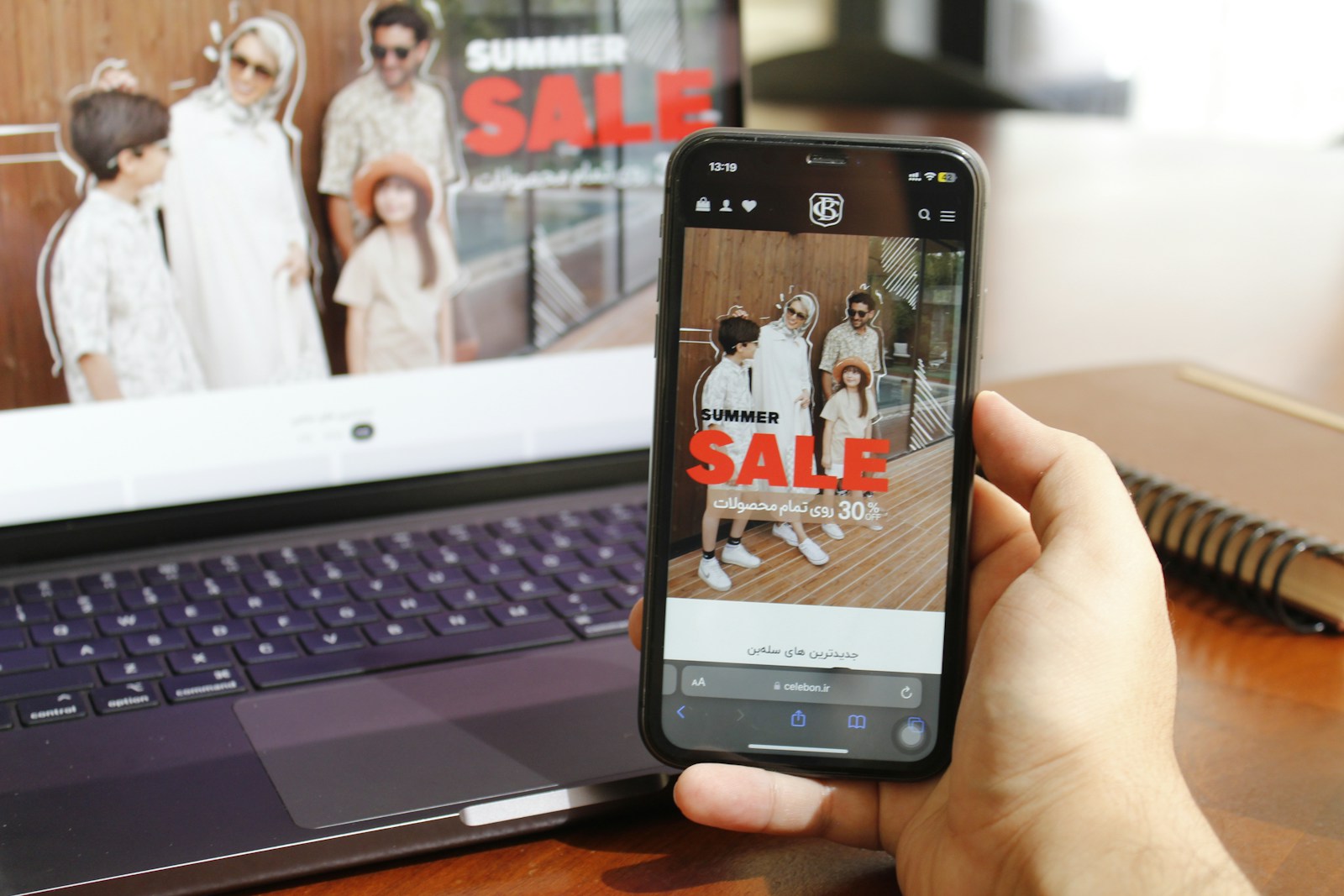 A person holding a cell phone in front of a laptop