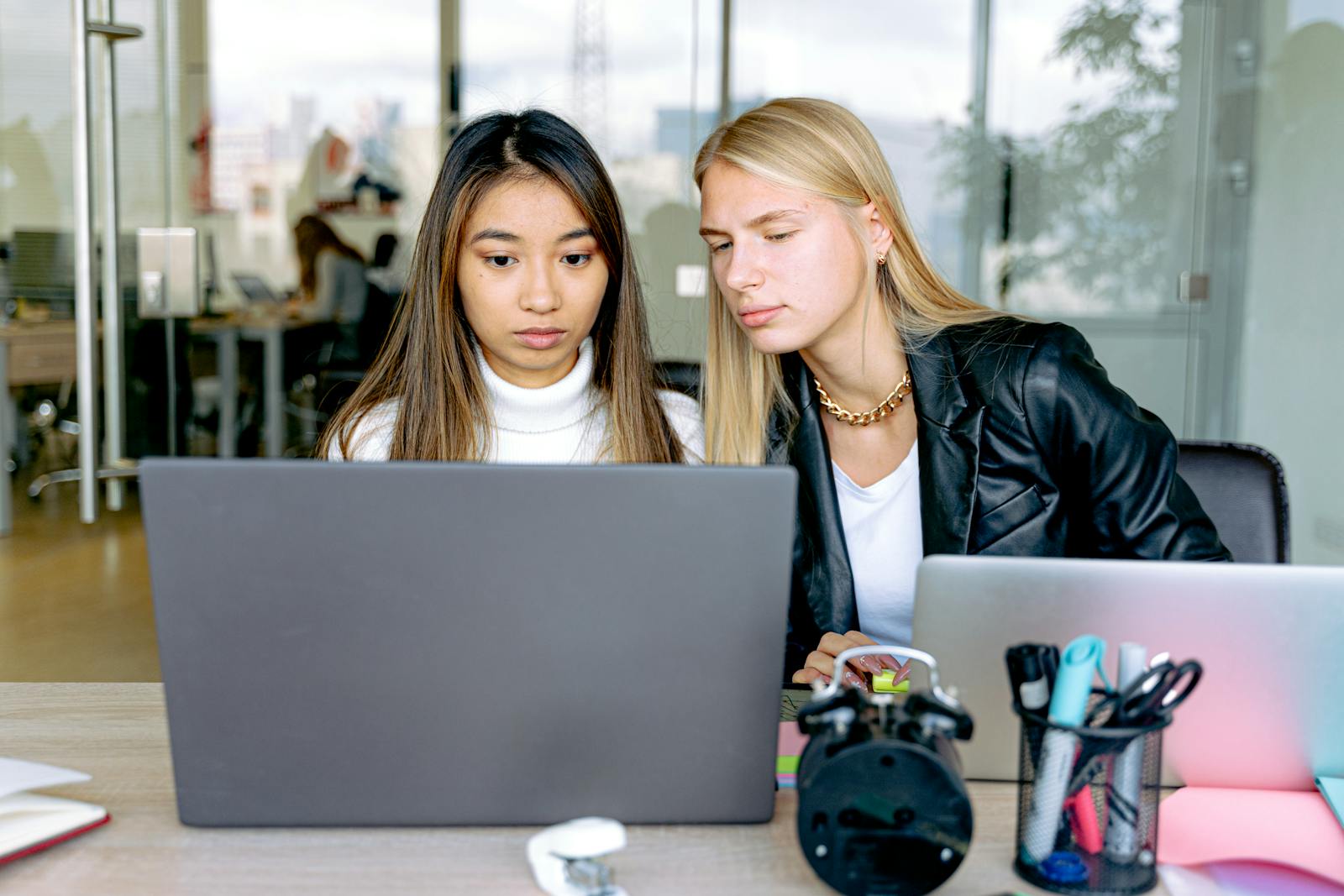 Two professional women working together on a laptop in a modern office setting.