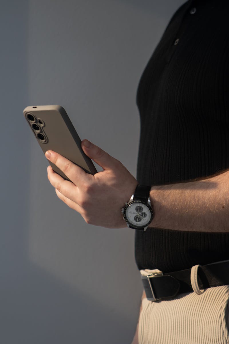 A casually dressed man looks at his smartphone indoors, showcasing modern style and technology.