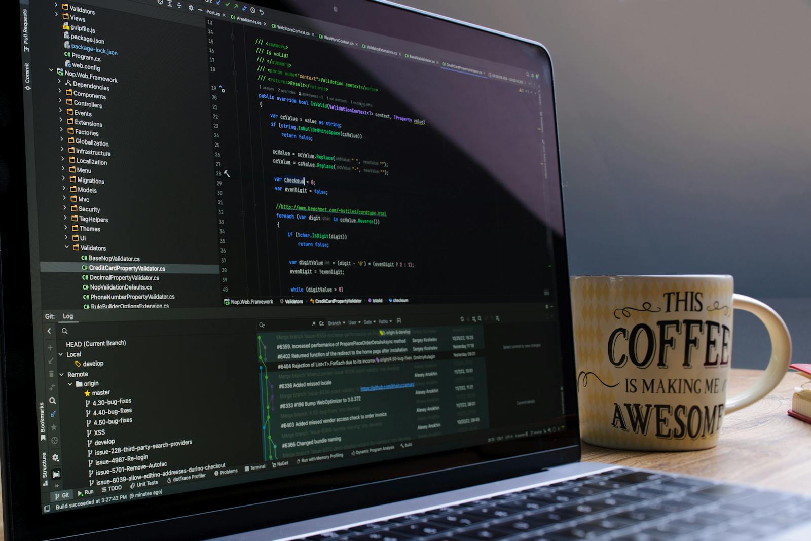 Close-up of laptop with coding software and a motivational coffee mug on a desk.