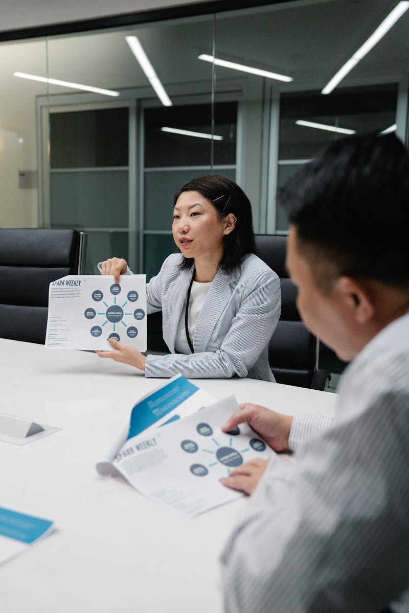 Two business professionals discussing documents in a modern conference room setting.