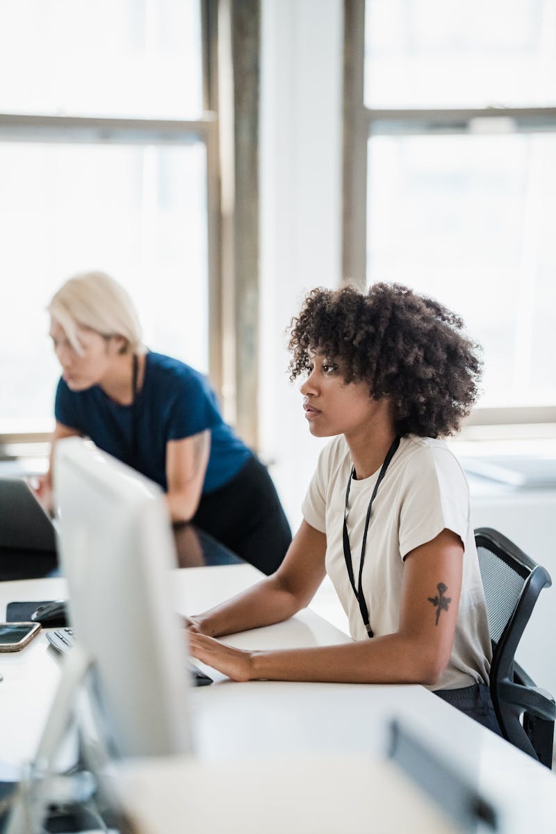 Two women working together in a modern, bright office setting, showcasing teamwork and collaboration.