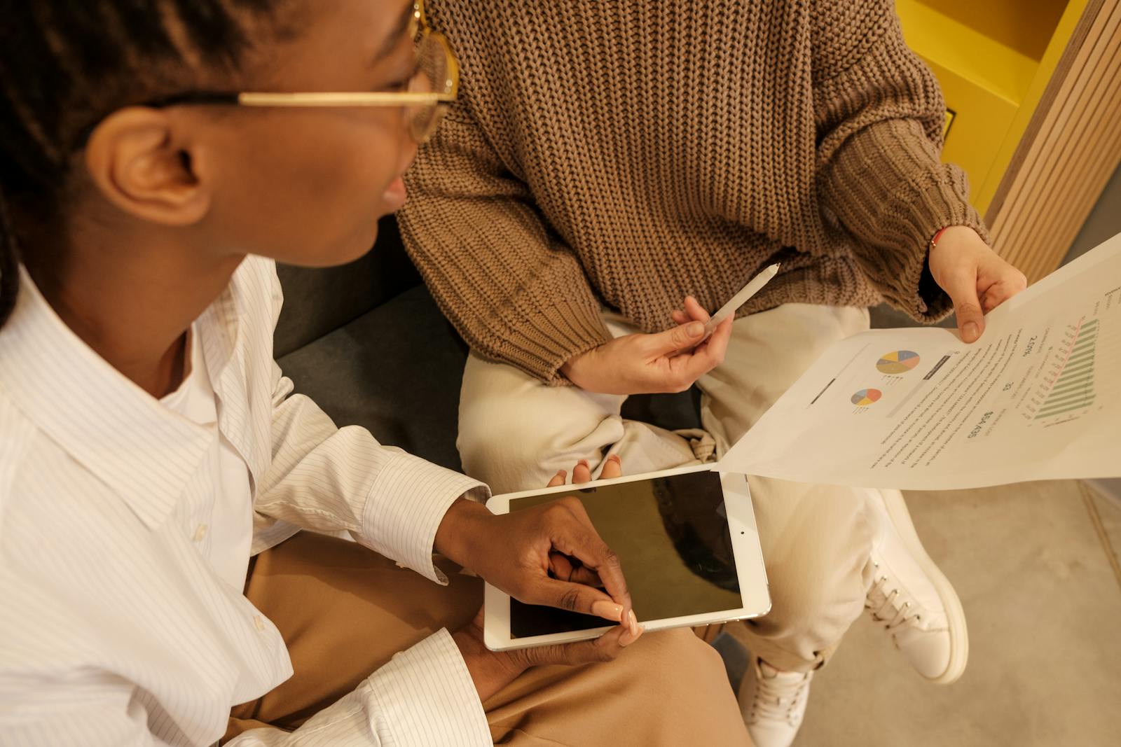 Two professionals discussing documents and data on a tablet during a business meeting.