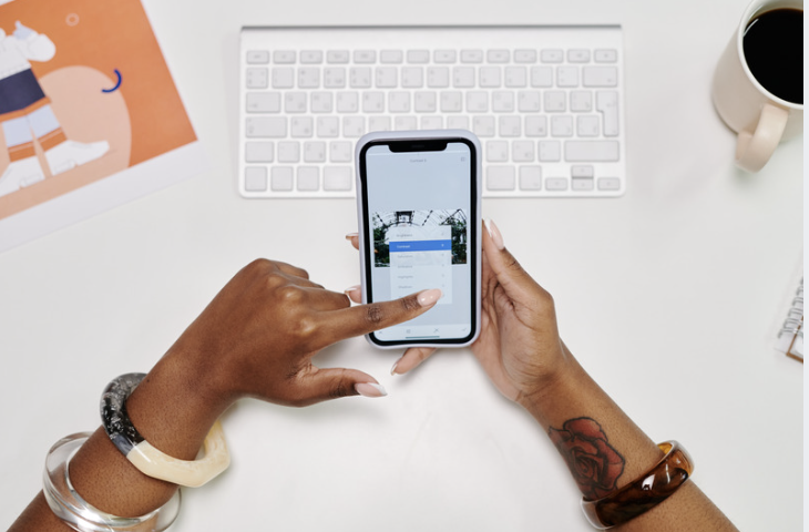 A person using a smartphone at a desk with a keyboard and workspace in the background, representing how progressive web apps deliver fast, responsive, app-like digital experiences across mobile and desktop devices without requiring a traditional app download.