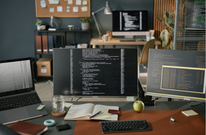 A modern software development workspace with multiple screens displaying code, system logs, and application interfaces, representing the tools, collaboration, and technical processes involved in Web application development.