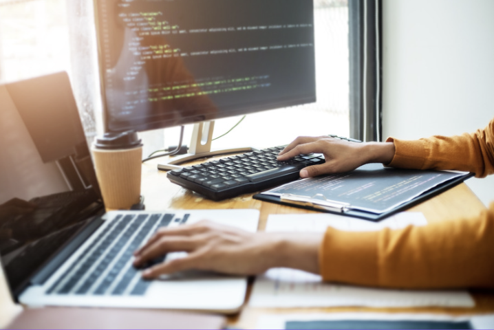 A developer working across multiple devices with code displayed on a monitor, laptop, and tablet, representing a website staging environment used to test updates, review functionality, identify issues, and verify changes before deploying them to a live website.